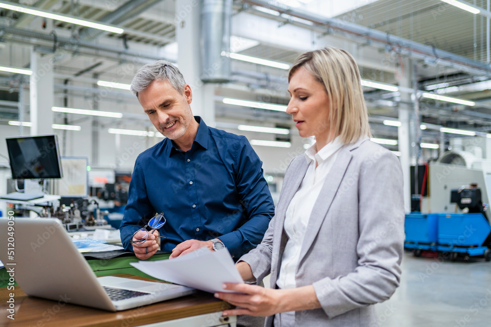 Businessman and businesswoman working on laptop together in factory Businessman and businesswoman working on laptop together in factory