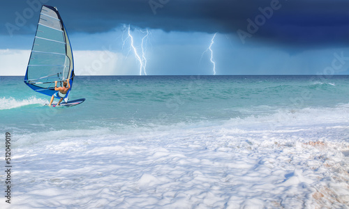Windsurfer surfing the wind on waves, strom and lightning in the background - Alacati, Cesme, Turkey 