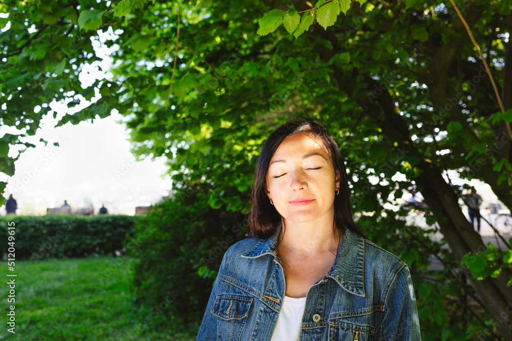 Woman wearing denim jacket with eyes closed in park Woman wearing denim jacket with eyes closed in park