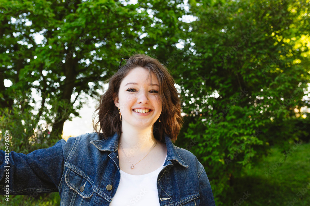 Smiling teenage girl wearing a denim jacket in front of bushes Smiling teenage girl wearing a denim jacket in front of bushes