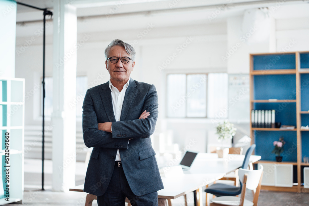 Smiling senior businessman standing with arms crossed in office Smiling senior businessman standing with arms crossed in office