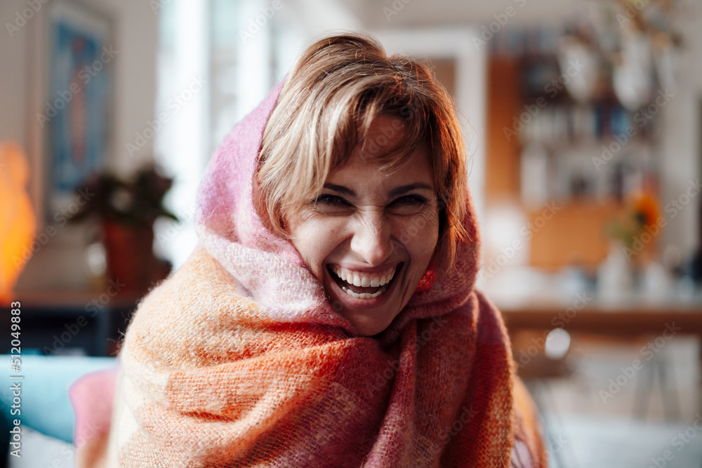 Cheerful woman wrapped in blanket sitting at home Cheerful woman wrapped in blanket sitting at home