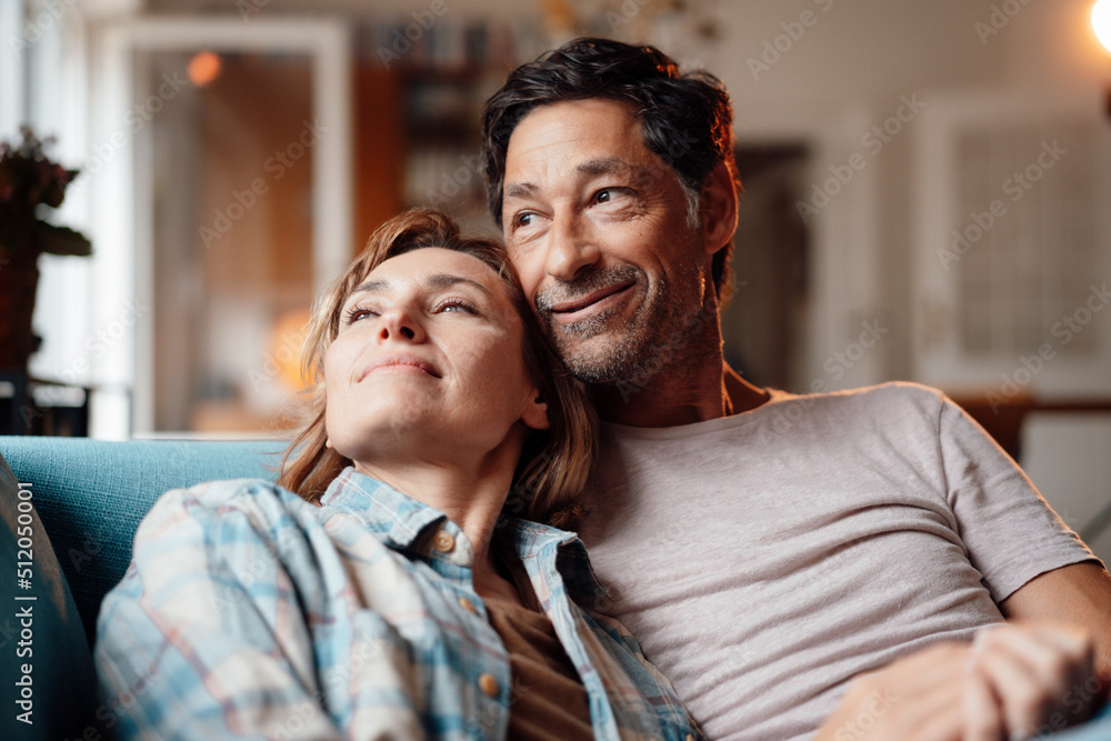 Smiling mature woman with man sitting on sofa at home Smiling mature woman with man sitting on sofa at home