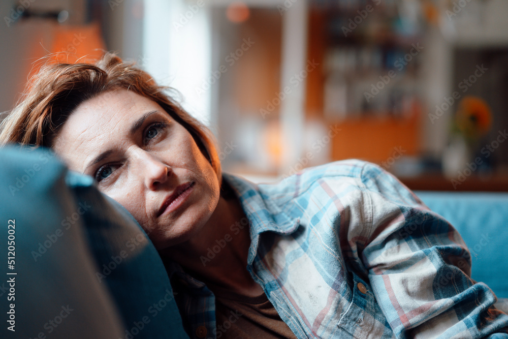 Thoughtful woman leaning on sofa in living room at home Thoughtful woman leaning on sofa in living room at home