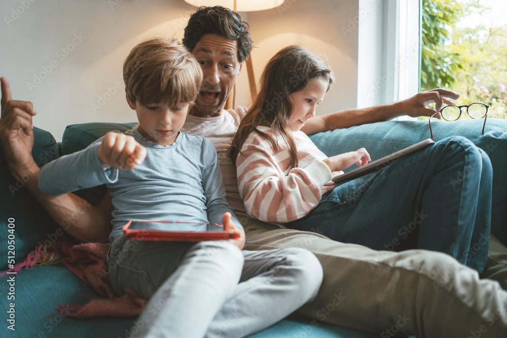 Happy father sitting with daughter and son using tablet PC at home Happy father sitting with daughter and son using tablet PC at home