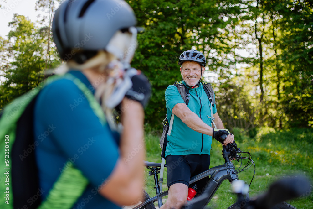 Obraz premium Active senior couple riding bicycles at summer park, woman is putting on helmet, healthy lifestyle concept.