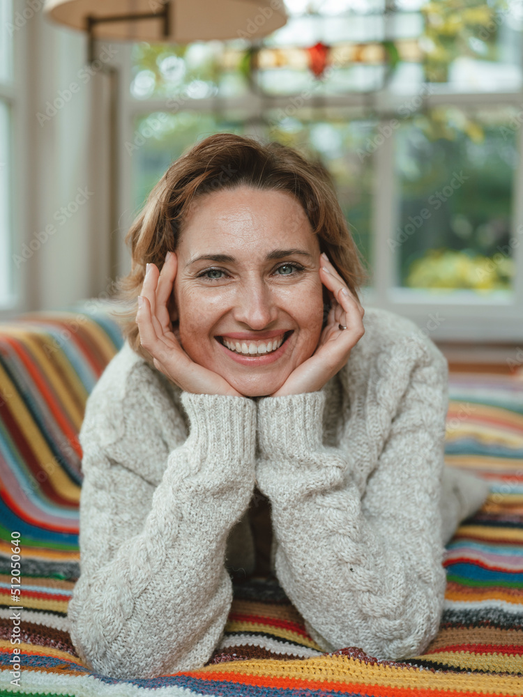 Happy mature woman wearing sweater lying on sofa at home Happy mature woman wearing sweater lying on sofa at home