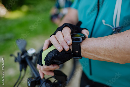 Close-up of senior man biker setting and looking at sports smartwatch, checking his performance.