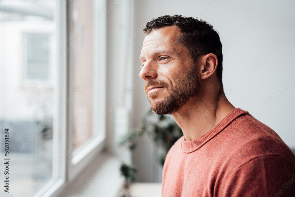 Smiling man looking out of window at home Smiling man looking out of window at home