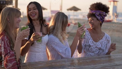 Young beautiful women drinking and dancing at cocktail party on the beach, female friends having fun at chiringuito during vacation, holiday activities, slow motion clip photo