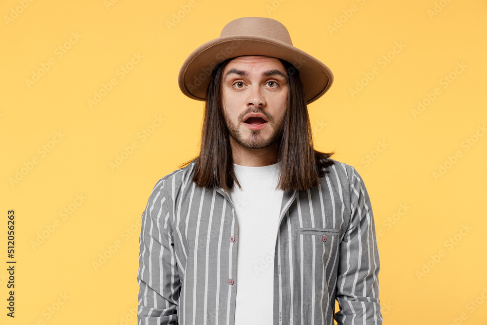 Young shocked surprised sad man he 20s wearing striped grey shirt white t-shirt hat look camera with opened mouth isolated on plain yellow color background studio portrait. People lifestyle concept. Young shocked surprised sad man he 20s wearing striped grey shirt white t-shirt hat look camera with opened mouth isolated on plain yellow color background studio portrait. People lifestyle concept.