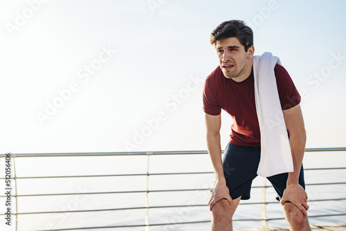 Young tired sad strong sporty athletic toned fit sportsman man 20s wear sports clothes lean on knees warm up training at sunrise sun dawn over sea beach outdoor on pier seaside in summer day morning. © ViDi Studio