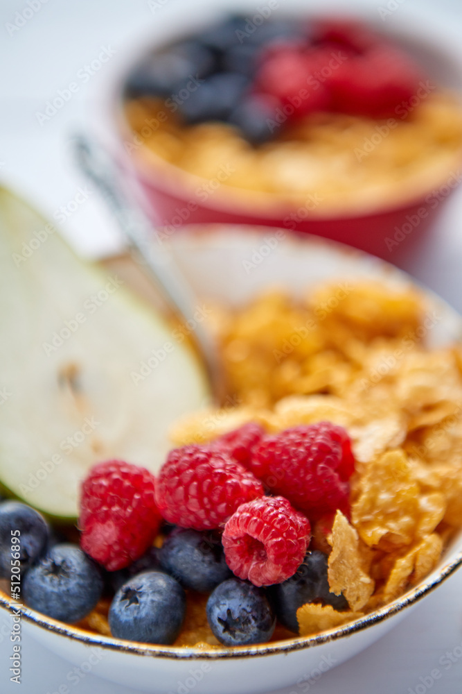 Golden cornflakes with fresh fruits of raspberries, blueberries and pear in ceramic bowl Golden cornflakes with fresh fruits of raspberries, blueberries and pear in ceramic bowl