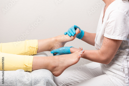 A pedicurist massages the client's feet. Close-up of legs and toenails with titanium thread and master's arms. The concept of chiropody and podology photo