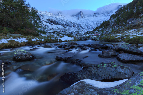 Mountain torrent at dusk in front snowy mountains, Valmasino, Valtellina, Lombardy, Italy photo
