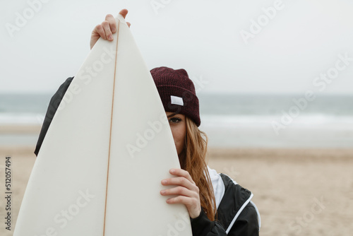 Girl with hat hides her face behind a surfboard