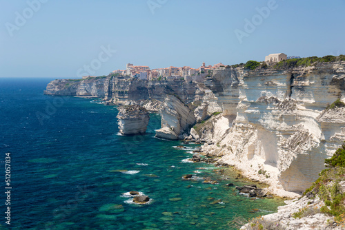 View over rocky cove along rugged limestone cliffs to the distant citadel, Bonifacio, Corse-du-Sud