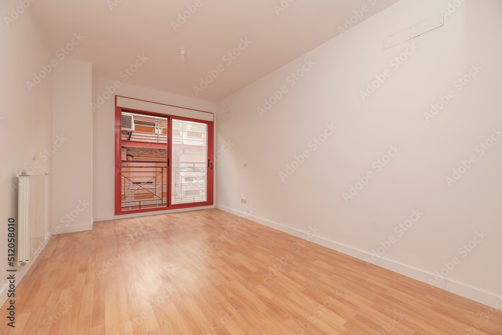 Empty room with white painted walls, oak parquet flooring, white aluminum radiator and reddish aluminum joinery on the sliding doors to the balcony Empty room with white painted walls, oak parquet flooring, white aluminum radiator and reddish aluminum joinery on the sliding doors to the balcony
