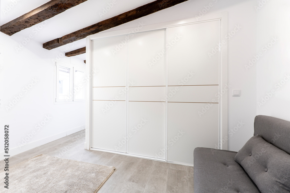 Fototapeta premium Wardrobe with three white sliding doors in a room with sloping ceilings and ceiling beams
