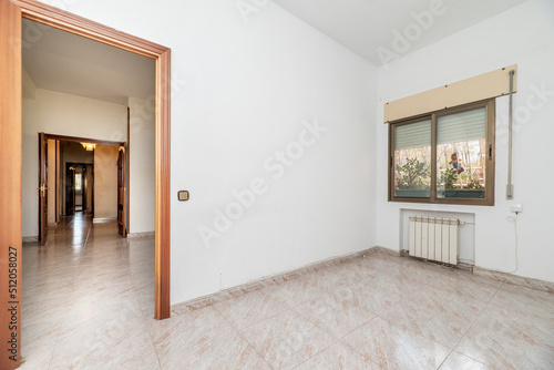 An empty room with white painted walls, ceramic tile floors, windows with plants and white aluminum radiators