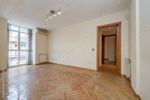 Empty room with light oak parquet  balcony with aluminum windows and radiator next to the window and white painted walls with oak carpentry