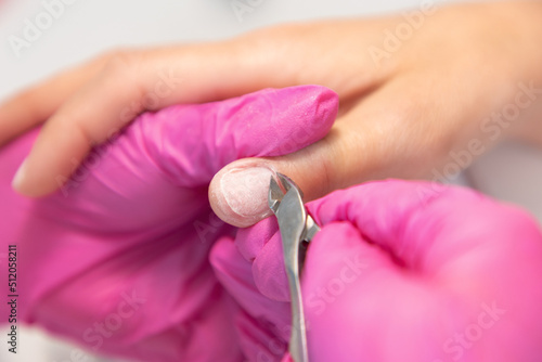 A master in medical pink gloves cuts off the cuticle with clippers. Close-up. The concept of manicure and salon nail care