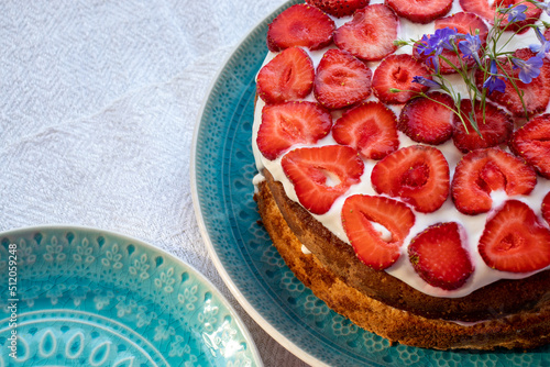 Cake with strawberries and cream on blue plate. Summer Strawberry and Cream sponge Layer Cake on white table cloth background. Top view, copy space. Midsummer food dessert