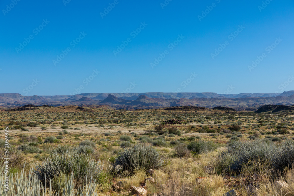 Semi arid landscape of the Augrabies National Park in the Northern Cape, South Africa.  Mountains and clear blu skies in the background. Grass and small shrubs in the foreground. 
