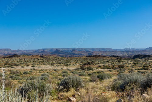 Semi arid landscape of the Augrabies National Park in the Northern Cape, South Africa. Mountains and clear blu skies in the background. Grass and small shrubs in the foreground. 