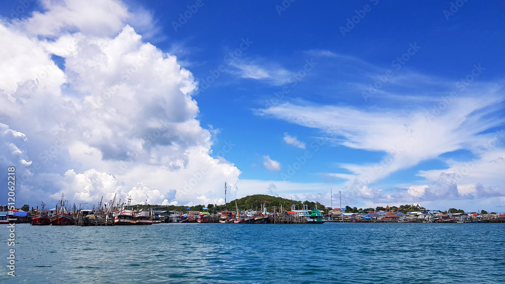 Many fishing boat parked on sea at port near coast and community with blue sky, white clouds and green mountain background and copy space. Landscape of ocean or seascape. Beautiful view and nature 