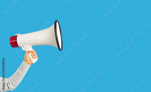 Hand with megaphone isolated on blue studio background making announcement. Person with loudspeaker attract attention for sale or offer. Advertising and promotion. Copy space.