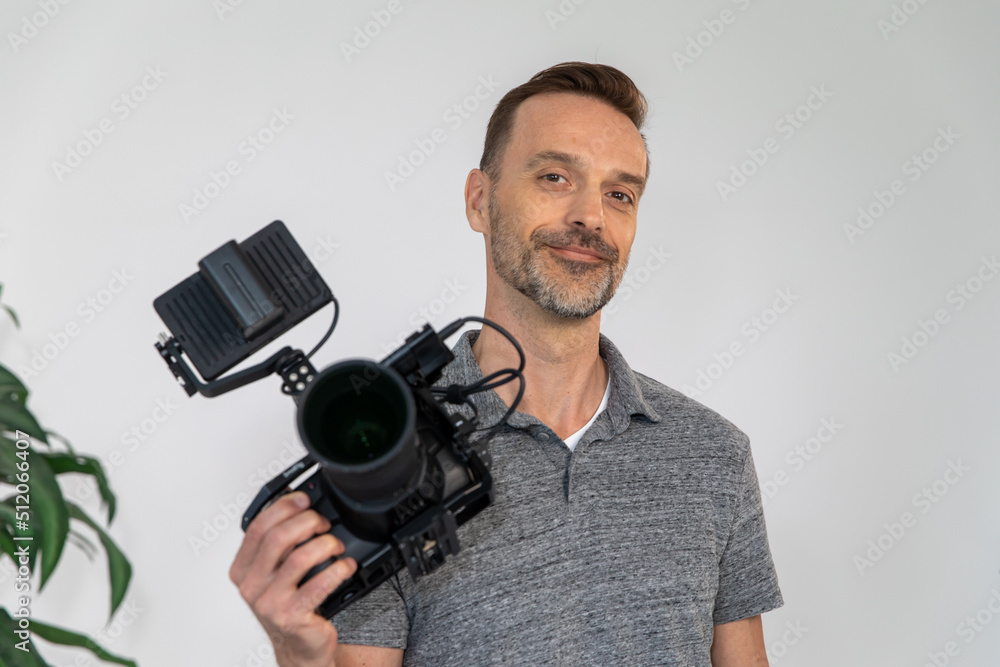Obraz premium Caucasian Videographer Posing with Video Camera in Hand on Film Set. Camera Man is Proud, Confident and Smiling Looking at Camera