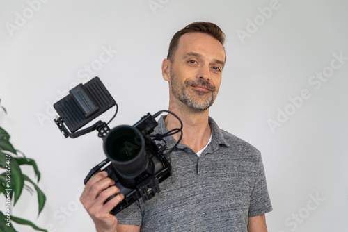 Caucasian Videographer Posing with Video Camera in Hand on Film Set. Camera Man is Proud, Confident and Smiling Looking at Camera