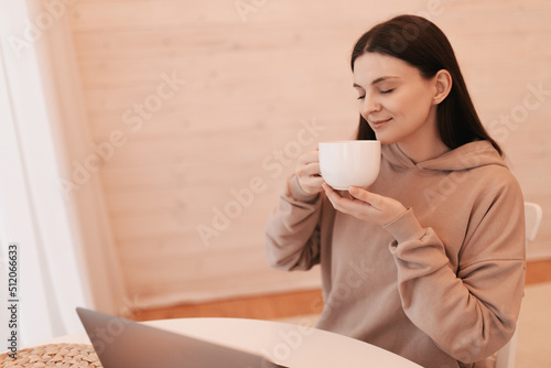 A woman is working remotely with laptop from her wooden house with a cup of tea.