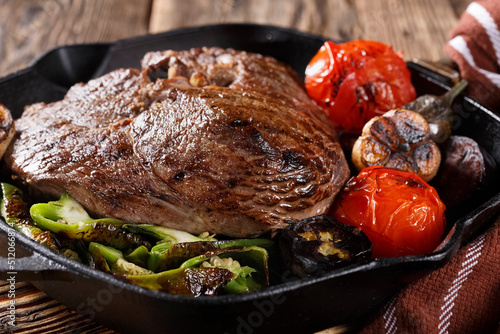 Large piece of grilled meat with vegetables in a cast iron pan, close-up, eating out, studio photo