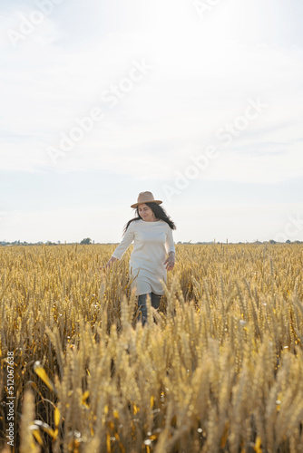 Mid adult woman in white dress standing on a wheat field with sunrise on the background, back view