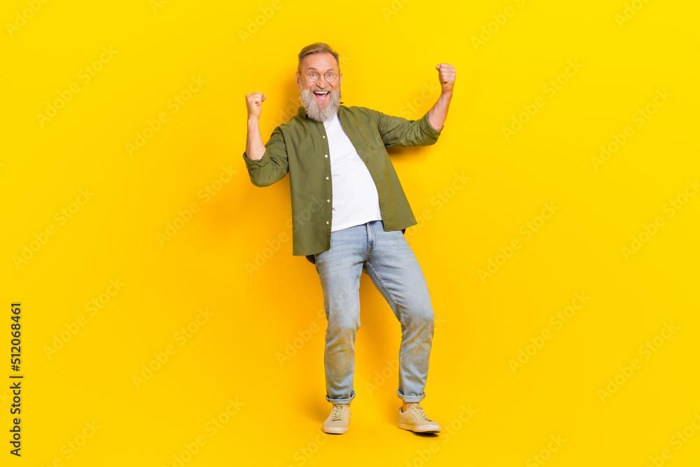 Full size portrait of delighted person raise fists celebrate success scream yeah hooray isolated on yellow color background Full size portrait of delighted person raise fists celebrate success scream yeah hooray isolated on yellow color background