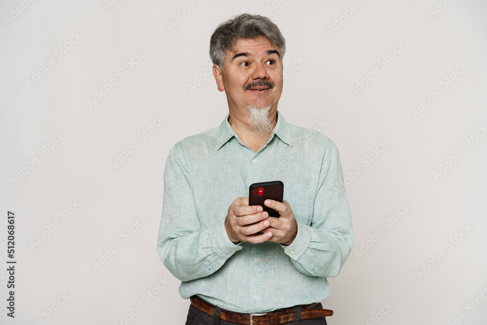 Mature man with grey beard smiling and using mobile phone Mature man with grey beard smiling and using mobile phone