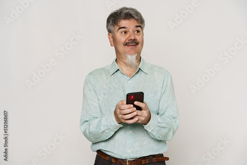 Mature man with grey beard smiling and using mobile phone