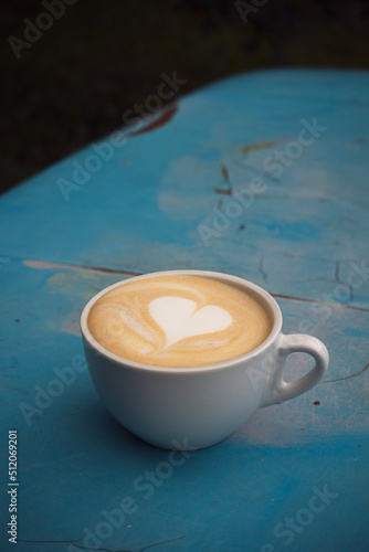 A cup of cappuccino with heart on a shabby blue surface.