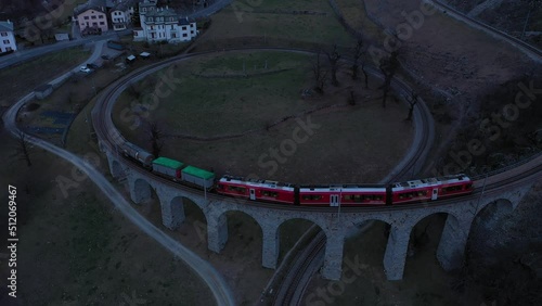 Train on Brusio Spiral Viaduct in Switzerland in the Evening. Bernina Railway. Swiss Alps. Aerial View. Drone Flies Backwards and Upwards photo