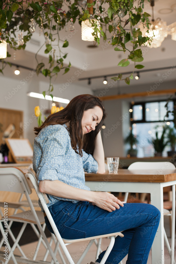 Young beautiful woman using mobile phone to browse social media sitting at cafe or coworkring space, smiling. Candid lifestyle photo of female using technology Young beautiful woman using mobile phone to browse social media sitting at cafe or coworkring space, smiling. Candid lifestyle photo of female using technology
