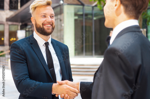 Handshake close-up. Businessman and his colleague are shaking hands in front of modern office building. Financial investors outdoor. Banking and business concept.