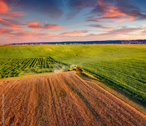 Beautiful summer scene of combine harvester on the field of wheat. Captivating summer view from flying drone of harvesting wheat on sunset. Picturesque rural scene on Ternopil outskirts, Ukraine.