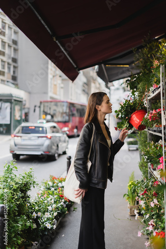 side view of woman with canvas shopper bag looking at green potted plants on street in paris. photo