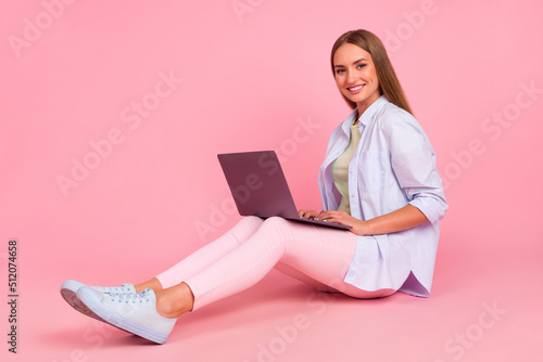 Full body portrait of pretty positive lady sitting floor use wireless netbook write email isolated on pink color background