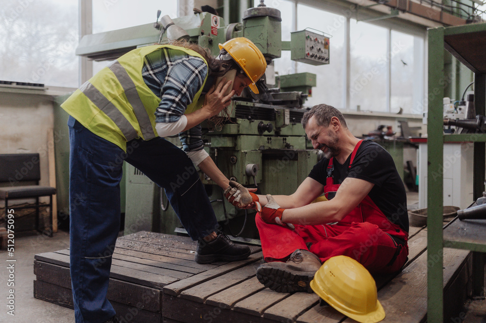 Woman is helping her colleague after accident in factory. First aid support on workplace concept. Woman is helping her colleague after accident in factory. First aid support on workplace concept.