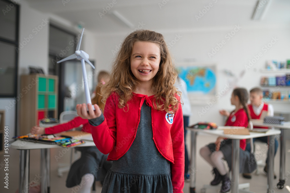 Schoolgirl holding wind turbine and learning about eco-friendly renewable sources of energy in classroom at school Schoolgirl holding wind turbine and learning about eco-friendly renewable sources of energy in classroom at school