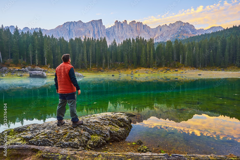 man stands on a stone by the lake, watching the sunrise over the mountains