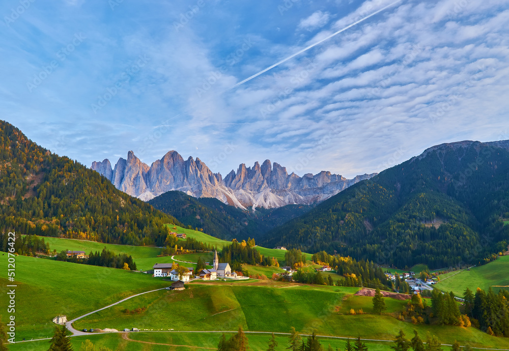 Amazing autumn scenery in Santa Maddalena village with church, colorful trees and meadows under rising sun rays. Dolomite Alps, Italy.